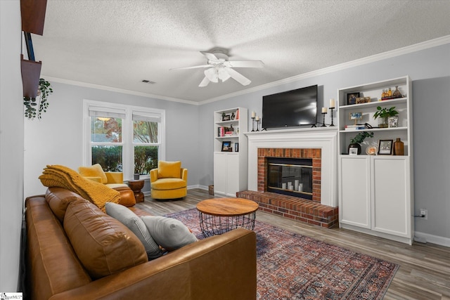 living room with ceiling fan, a brick fireplace, crown molding, wood-type flooring, and a textured ceiling