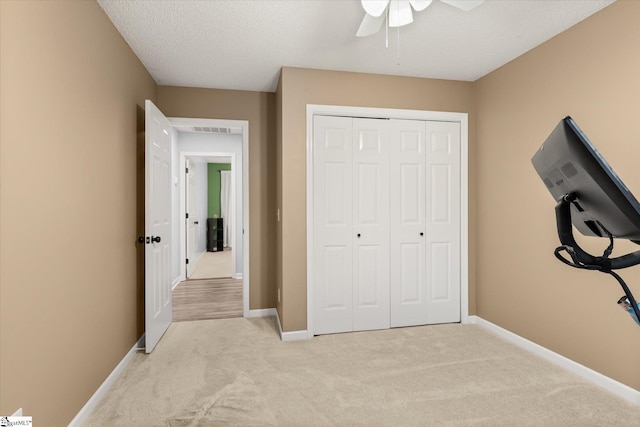 unfurnished bedroom with light carpet, a textured ceiling, a closet, and ceiling fan