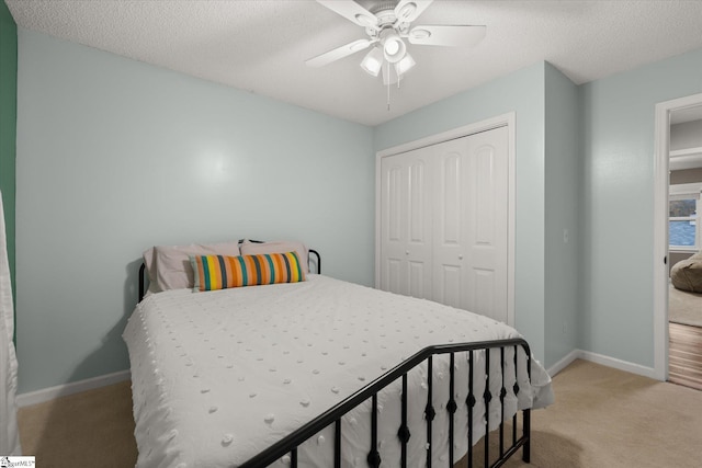 bedroom featuring a textured ceiling, a closet, light colored carpet, and ceiling fan