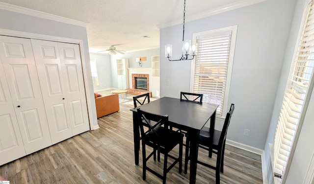 dining space featuring ceiling fan with notable chandelier, crown molding, a textured ceiling, a fireplace, and wood-type flooring