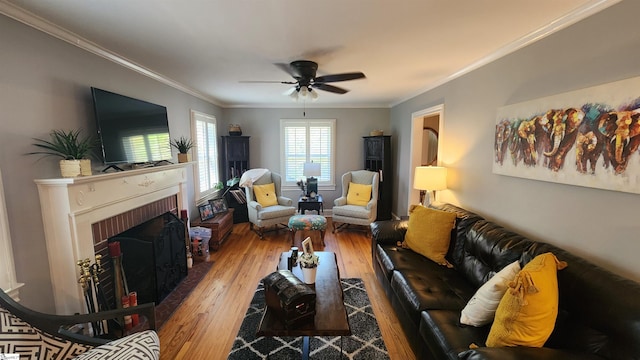 living room featuring hardwood / wood-style floors, ceiling fan, crown molding, and a brick fireplace