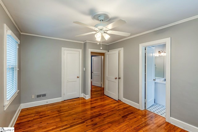 unfurnished bedroom featuring ensuite bathroom, multiple windows, hardwood / wood-style flooring, and ceiling fan