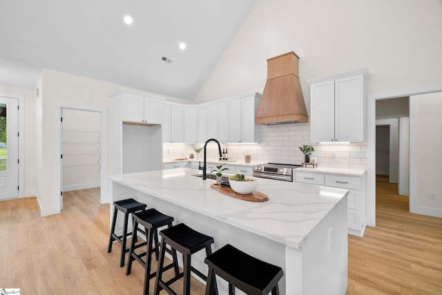 kitchen featuring white cabinetry, custom range hood, and a center island with sink