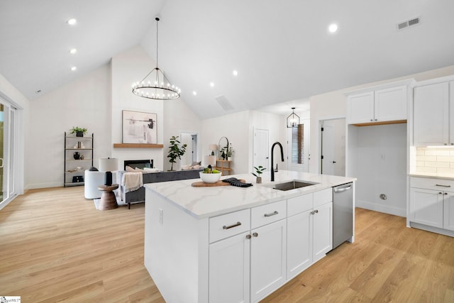 kitchen with light wood-type flooring, white cabinetry, sink, and a kitchen island with sink