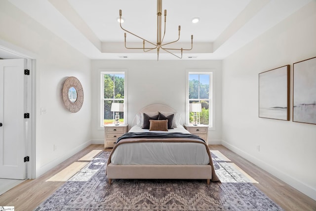 bedroom with a chandelier, multiple windows, light hardwood / wood-style floors, and a raised ceiling