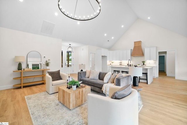 living room featuring an inviting chandelier, sink, light hardwood / wood-style flooring, and high vaulted ceiling