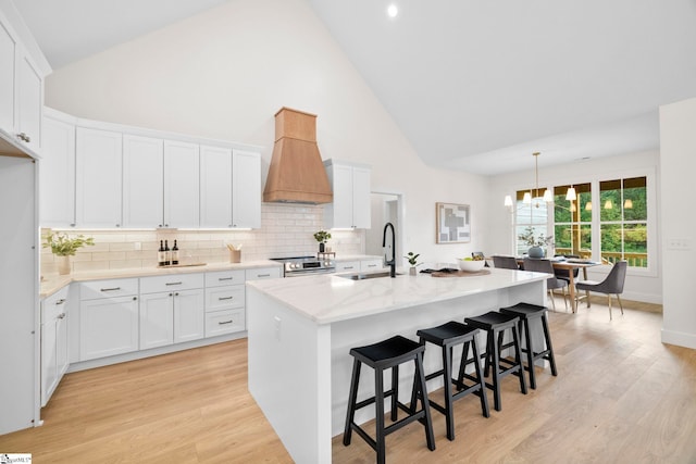 kitchen with an island with sink, white cabinetry, sink, and high vaulted ceiling