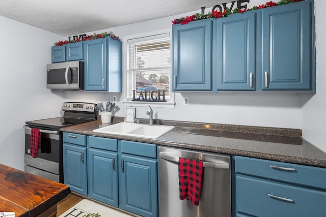 kitchen with sink, appliances with stainless steel finishes, a textured ceiling, blue cabinetry, and light wood-type flooring