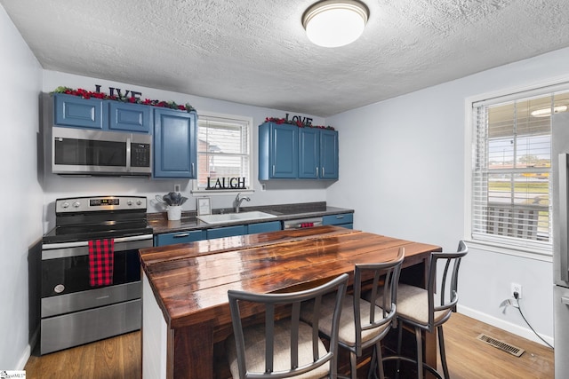 kitchen with blue cabinets, appliances with stainless steel finishes, a textured ceiling, and light hardwood / wood-style floors