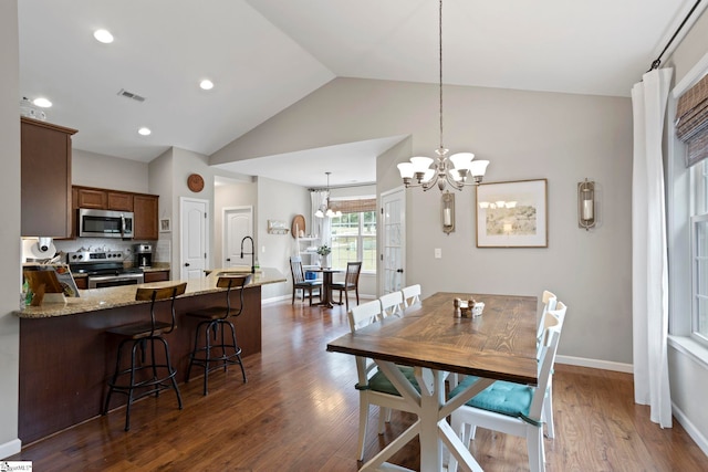 dining space with dark hardwood / wood-style flooring, an inviting chandelier, sink, and vaulted ceiling