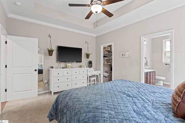 bedroom with ensuite bath, light colored carpet, ceiling fan, a raised ceiling, and a spacious closet