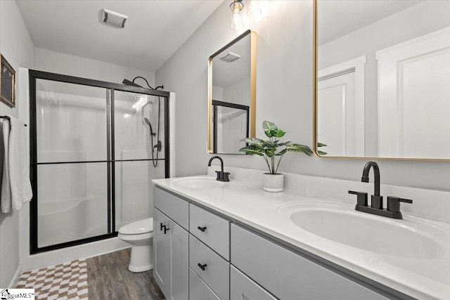 bathroom with hardwood / wood-style floors, a shower with door, vanity, and toilet