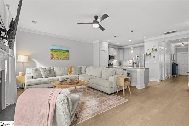 living room with ornamental molding, ceiling fan, sink, and light hardwood / wood-style floors