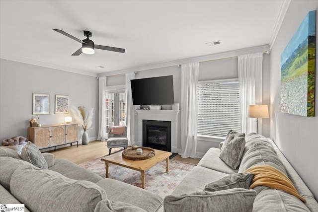 living room featuring light hardwood / wood-style floors, a healthy amount of sunlight, crown molding, and ceiling fan