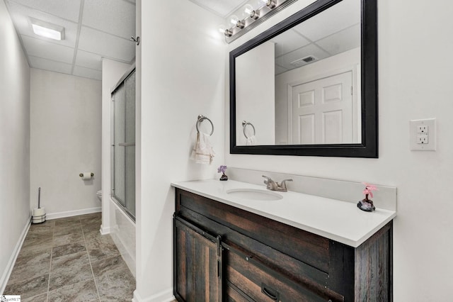 bathroom featuring a paneled ceiling, vanity, and bath / shower combo with glass door