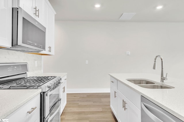 kitchen with white cabinets, stainless steel appliances, sink, and light hardwood / wood-style flooring