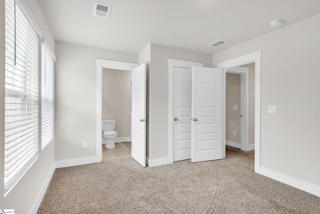 unfurnished bedroom featuring ensuite bathroom, multiple windows, and light carpet