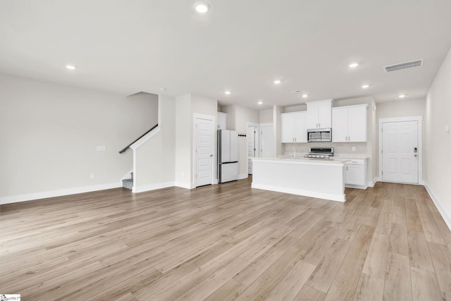 kitchen featuring a kitchen island with sink, white cabinetry, appliances with stainless steel finishes, backsplash, and light hardwood / wood-style flooring