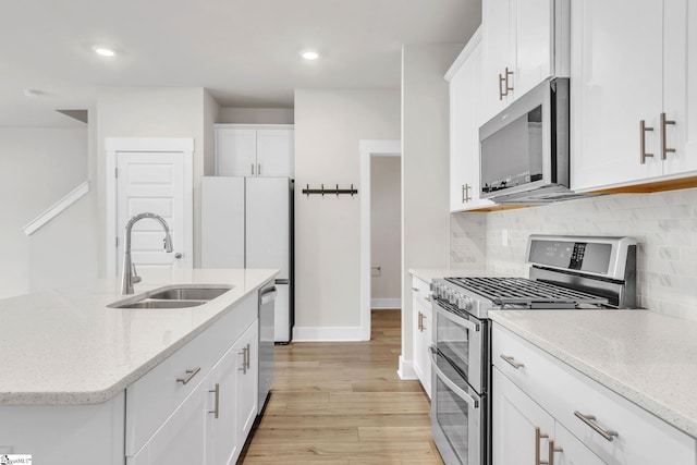 kitchen with light hardwood / wood-style floors, light stone counters, white cabinets, sink, and appliances with stainless steel finishes