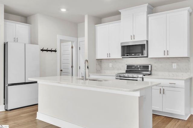 kitchen with white cabinets, sink, a kitchen island with sink, light wood-type flooring, and appliances with stainless steel finishes