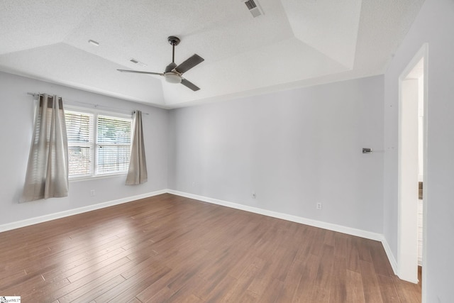 unfurnished room featuring ceiling fan, a textured ceiling, a raised ceiling, lofted ceiling, and dark wood-type flooring