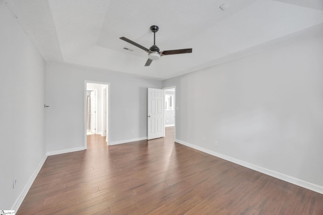 unfurnished bedroom with dark hardwood / wood-style flooring, a textured ceiling, ceiling fan, and a raised ceiling