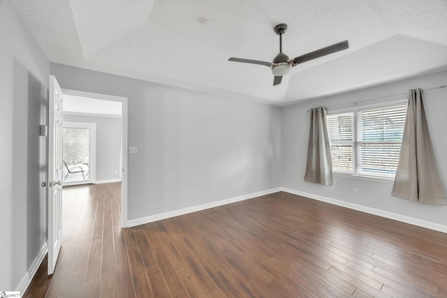 empty room with ceiling fan, a textured ceiling, dark hardwood / wood-style flooring, and a tray ceiling