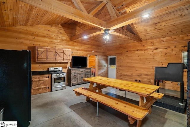 kitchen featuring wood walls, beam ceiling, wood ceiling, stainless steel gas range oven, and black refrigerator