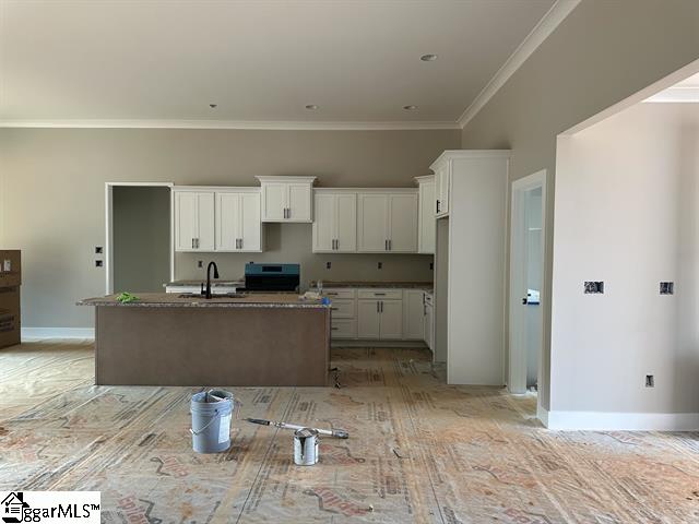 kitchen featuring ornamental molding, dark stone counters, white cabinetry, sink, and a kitchen island with sink