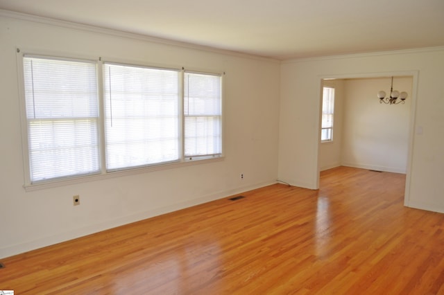 empty room with plenty of natural light, a notable chandelier, crown molding, and light hardwood / wood-style flooring