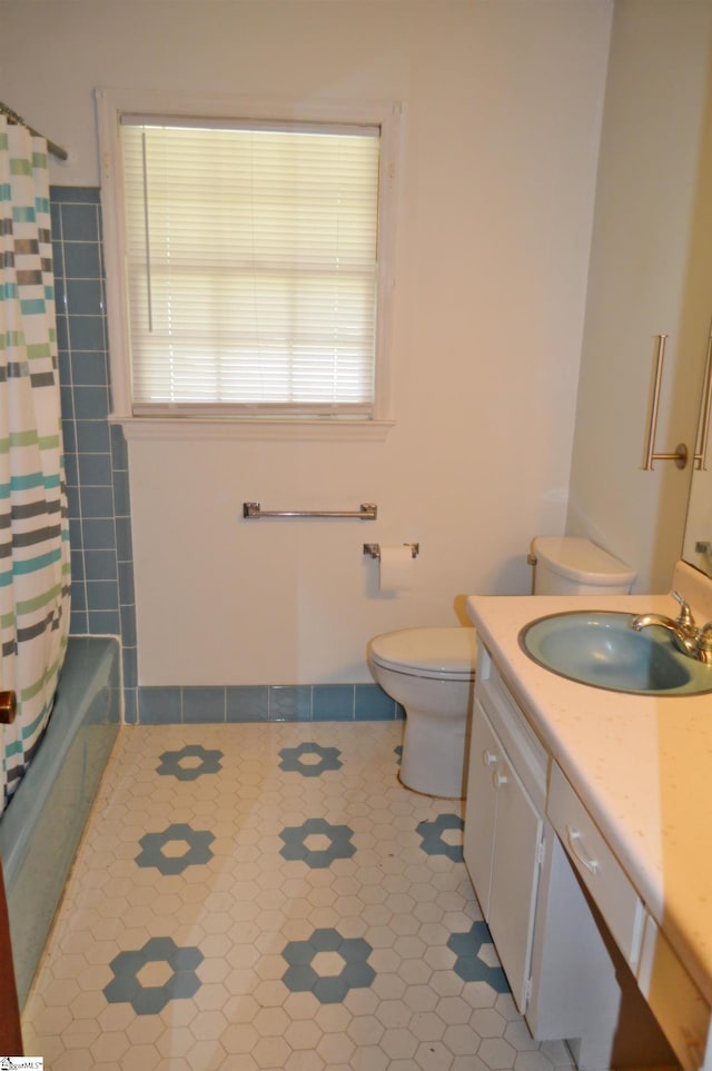 full bathroom with shower / bathtub combination with curtain, vanity, tile patterned floors, toilet, and tile walls