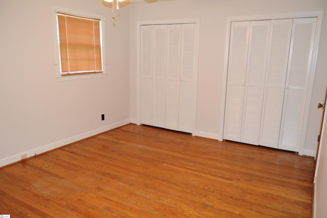 unfurnished bedroom featuring hardwood / wood-style flooring and multiple closets