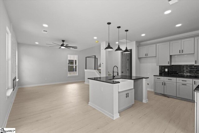 kitchen with gray cabinetry, ceiling fan, sink, light hardwood / wood-style flooring, and an island with sink