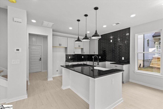 kitchen featuring a center island with sink, light hardwood / wood-style flooring, hanging light fixtures, and sink