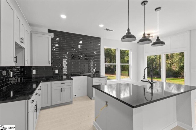 kitchen featuring decorative backsplash, decorative light fixtures, a center island with sink, white cabinets, and light hardwood / wood-style floors