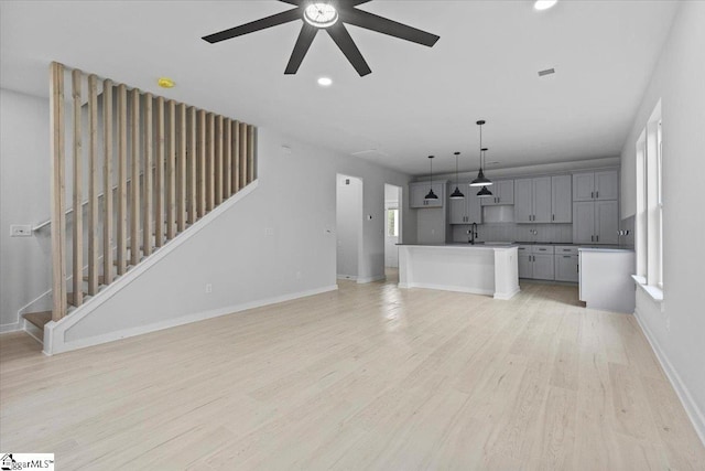 unfurnished living room featuring ceiling fan, sink, and light wood-type flooring