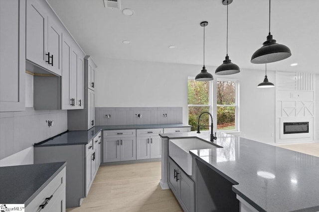 kitchen with decorative backsplash, light wood-type flooring, sink, decorative light fixtures, and dark stone countertops