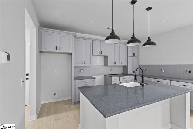 kitchen featuring a center island with sink, hanging light fixtures, light hardwood / wood-style floors, and sink