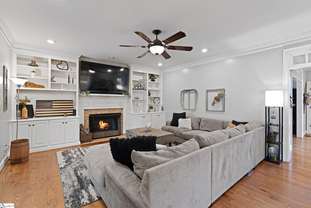 living room with light hardwood / wood-style floors, built in shelves, ceiling fan, crown molding, and a fireplace