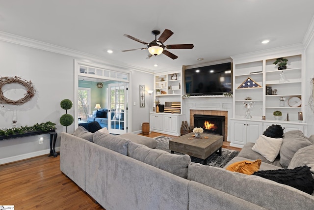 living room with ornamental molding, a fireplace, hardwood / wood-style flooring, and ceiling fan