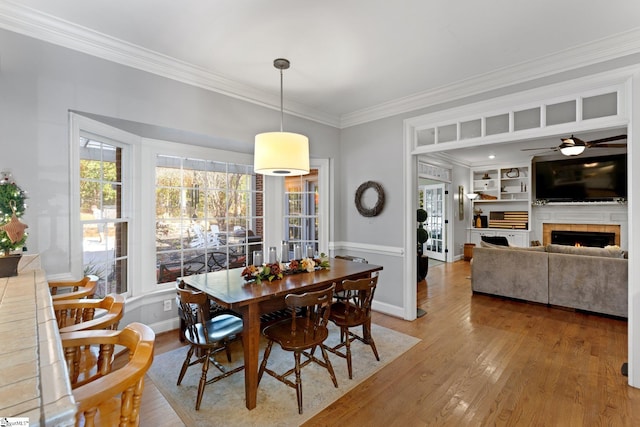 dining room with hardwood / wood-style flooring, ceiling fan, crown molding, built in features, and a tile fireplace