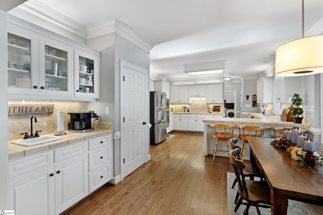 kitchen with ornamental molding, stainless steel fridge, sink, light hardwood / wood-style floors, and white cabinets