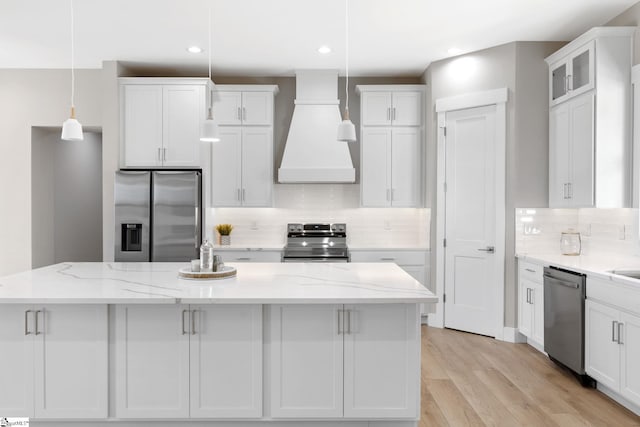 kitchen featuring white cabinets, custom range hood, a kitchen island, pendant lighting, and appliances with stainless steel finishes