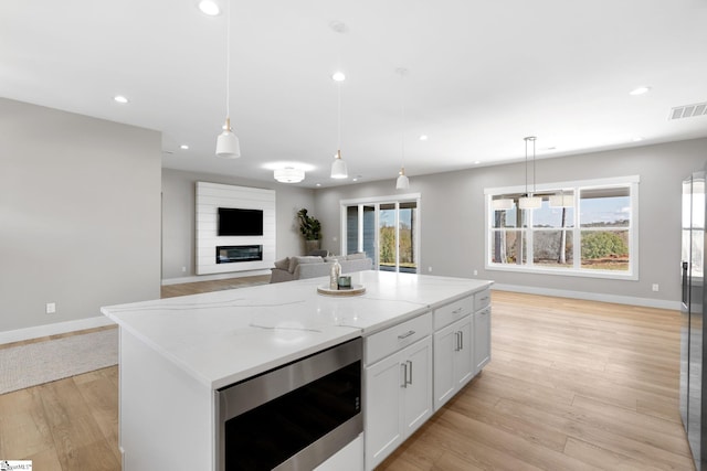 kitchen featuring pendant lighting, light stone countertops, a center island, white cabinets, and light wood-type flooring