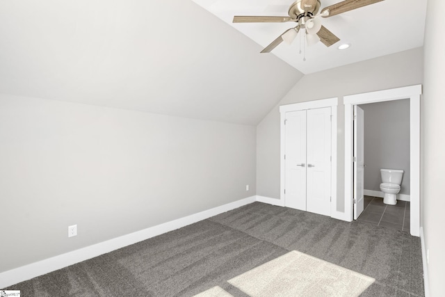 unfurnished bedroom featuring ensuite bath, vaulted ceiling, dark carpet, ceiling fan, and a closet