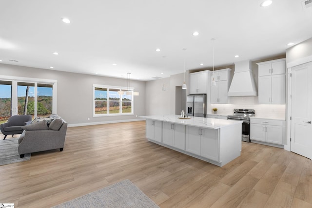 kitchen featuring premium range hood, stainless steel appliances, light wood-type flooring, white cabinetry, and a kitchen island with sink