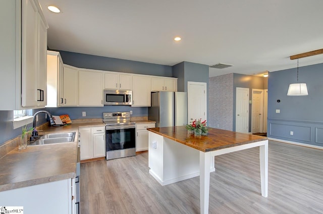 kitchen with stainless steel appliances, white cabinets, sink, pendant lighting, and light hardwood / wood-style flooring