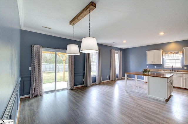 kitchen featuring wood-type flooring, white cabinets, a kitchen island, crown molding, and decorative light fixtures