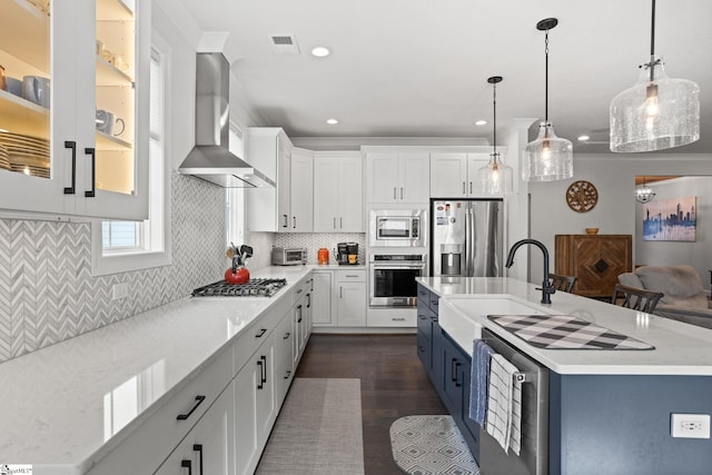 kitchen featuring white cabinetry, sink, appliances with stainless steel finishes, wall chimney range hood, and pendant lighting