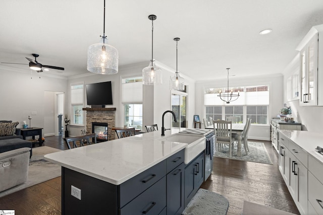 kitchen featuring a stone fireplace, white cabinetry, decorative light fixtures, dark wood-type flooring, and a kitchen island with sink